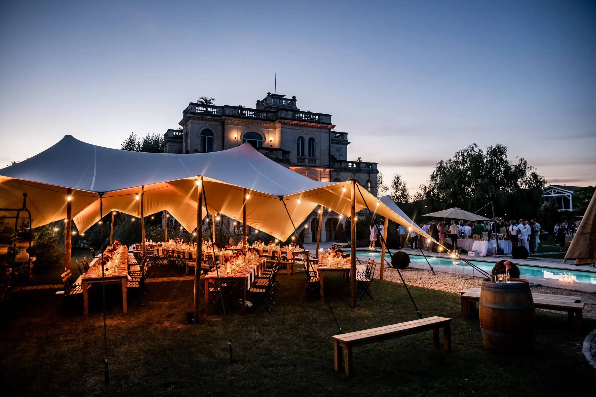 Réception de mariage en soirée sous tente lumineuse devant un château