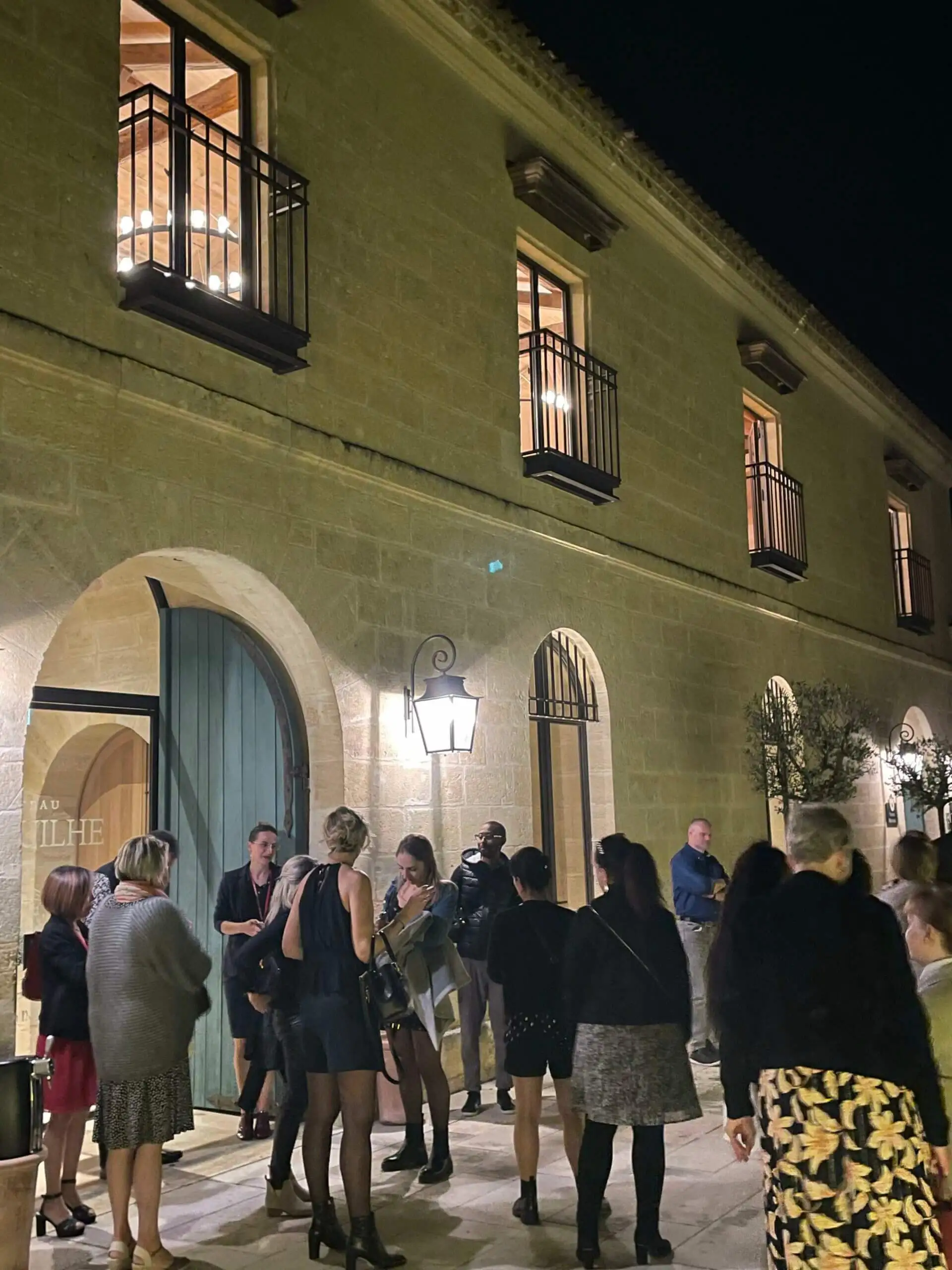 Cocktail en extérieur devant une bâtisse en pierre éclairée, invités debout
